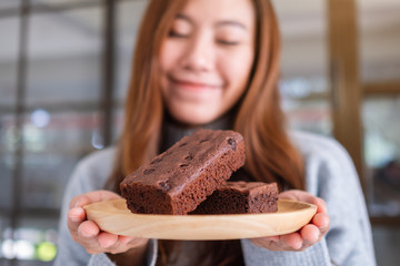 Closeup image of a beautiful asian woman holding a brownie cake in wooden plate