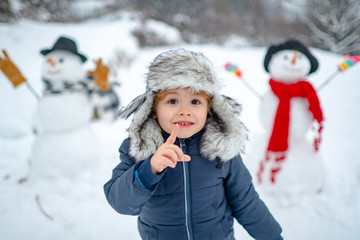 Fototapeta na wymiar Merry Christmas and Happy new year. Winter portrait of little boy child in snow Garden make snowman. Cute kid - winter portrait. Winter clothes for kids.