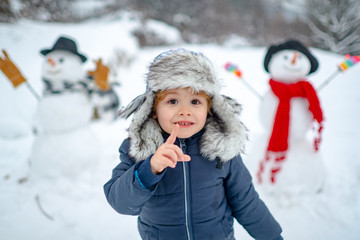 Merry Christmas and Happy new year. Winter portrait of little boy child in snow Garden make snowman. Cute kid - winter portrait. Winter clothes for kids.