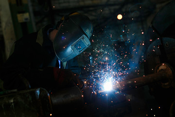 Welding work. Worker welds metal parts by electric welding at the factory.