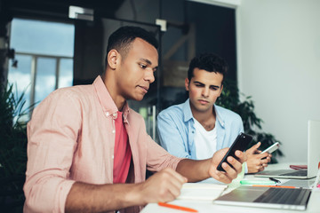 Multicultural male colleagues browsing info from mobile platform for millennials checking notification for install, young diverse employees reading market news on social website connected to 4g