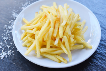 Fresh french fries and salt in white plate with black background - Tasty potato fries for food or snack delicious Italian meny homemade ingredients