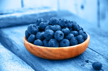Heap of fresh ripe raw bluberries in a small wooden plate toned in trendy color.