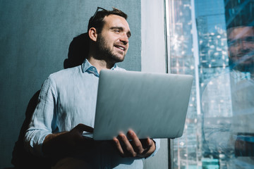 Successful male office worker holding laptop computer with 4g wireless internet and looking in...