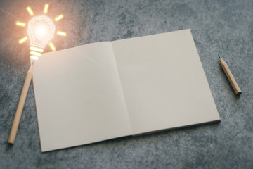 Pencils and plain notebook with light bulb futuristic icon on black background with copy space....