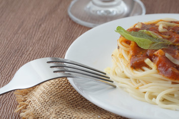 View of spagetti bolognese with green basil on top over brown background. Silver fork placed next to the white plate.