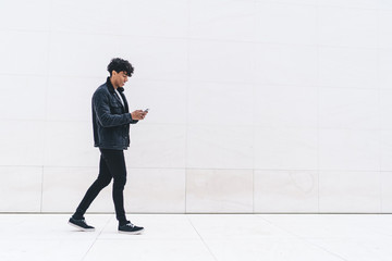 Modern adult curly male in casual outfit browsing mobile while walking on marble passage