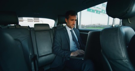 Slow motion of handsome businessman using his laptop during traveling in a modern car with a driver in center of the city by day.Shot in 8K. Concept of business, success, traveling, luxury - Powered by Adobe