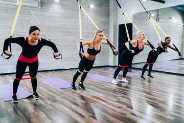 Multiracial young slim females exercising with push ups and expander