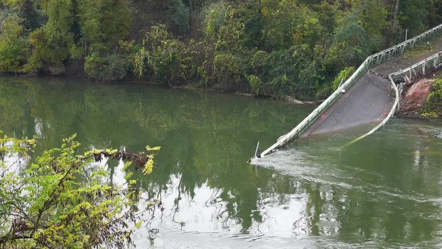 Broken metal bridge beetween two shores . The remains of the bridge protrude from the ground on the other side and hide under water in rainy gray weather. France.