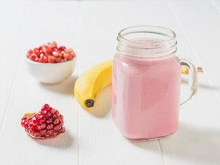 A mug of pomegranate banana smoothie and fresh fruit on a white table. 