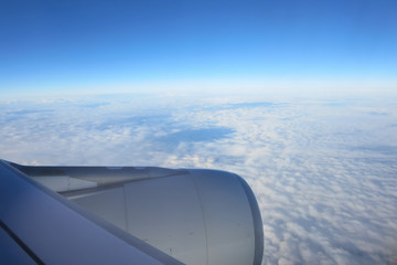 Airplane's wing, beautiful clouds, and blue sky through a window of airplane.