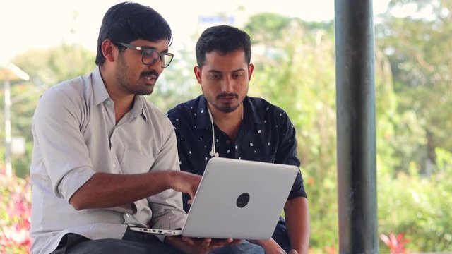 Two Students Discussing at College campus on laptop - Concept of young people using technology for learning - young man explaining to his colleague by looking on the computer.