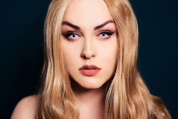 Blonde with long hair looking at the camera. Professional makeup, beautiful eyebrows, white lenses. Looking vampires, bright eyes. Hair care. Blindinka on a black back