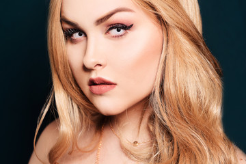 Fototapeta premium Blonde with long hair looking at the camera. Professional makeup, beautiful eyebrows, white lenses. Looking vampires, bright eyes. Hair care. Blindinka on a black back