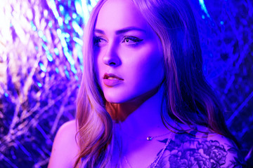 Gorgeous blonde in neon color, red-blue color, abstract background. Girl with white lenses. Club photo. Girl with a flower tattoo on his shoulder.