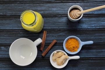Obraz na płótnie Canvas Turmeric latte, golden milk or the anti-inflammatory Indian Haldi Doodh with superfood Turmeric powder, Ginder and Cinnamon sweetened with honey on wooden background