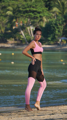 tanned sporty girl in pink yoga pants on sunny beach, beautiful day in tropics