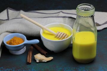 Turmeric latte, golden milk or the anti-inflammatory Indian Haldi Doodh with superfood Turmeric powder, Ginder and Cinnamon sweetened with honey on wooden background