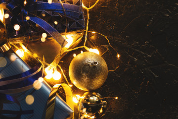 Christmas gift with blue ribbon and Christmas decoration balls on abstract bokeh black background with copy space and decorative LED lights. Merry Christmas and New Year.