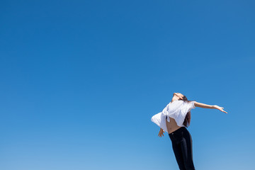 Happy woman with tanned slim body breathing fresh air raising her arms up, enjoying a sunny summer holiday on beach destination against blue sky, outdoors. Travel and well being lifestyle.
