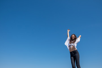 Fototapeta na wymiar Happy woman with tanned slim body breathing fresh air raising her arms up, enjoying a sunny summer holiday on beach destination against blue sky, outdoors. Travel and well being lifestyle.