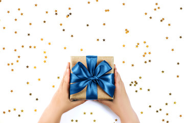 Child's hands holding present with blue bow on white rustic sparkling background. Festive backdrop for Birthday, Valentines day, Christmas, New Year. Flat lay style.