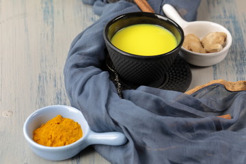 Turmeric latte, golden milk or the anti-inflammatory Indian Haldi Doodh with superfood Turmeric powder, Ginder and Cinnamon sweetened with honey on wooden background