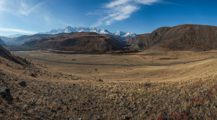 Mountain landscape. Spacious valley, snowy ridge and blue sky with white clouds.