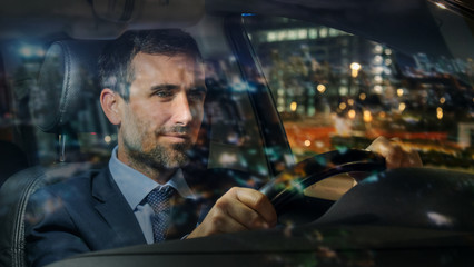 An young handsome businessman driving a modern car in center of the city by night. Concept of business, success, traveling, luxury
