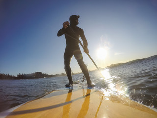 Adventurous Man Surfer on a paddle board is surfing in the ocean during a sunny morning in Fall Season. Taken in Long Beach, Tofino, Vancouver Island, BC, Canada.