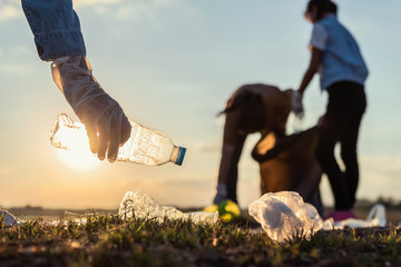 people volunteer keeping garbage plastic bottle into black bag at park river in sunset