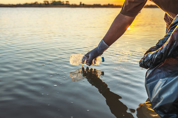 people volunteer keeping garbage plastic bottle into black bag on river in sunset