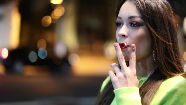 Young woman smoking and walking at night in city