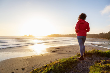 Long Beach, Near Tofino and Ucluelet in Vancouver Island, BC, Canada. Adventurous Girl standing and watching the golden sunset on the Pacific Ocean Coast.