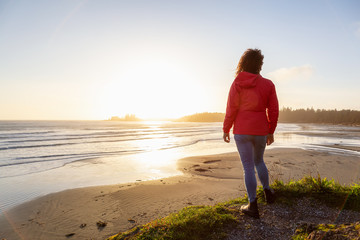 Long Beach, Near Tofino and Ucluelet in Vancouver Island, BC, Canada. Adventurous Girl standing and watching the golden sunset on the Pacific Ocean Coast.