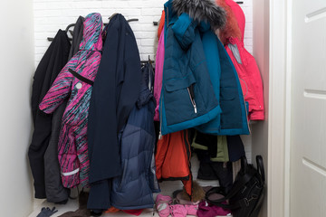 a lot of winter clothes hanging on a hanger in the hallway. jackets, gloves, pants, jumpsuit, bag...