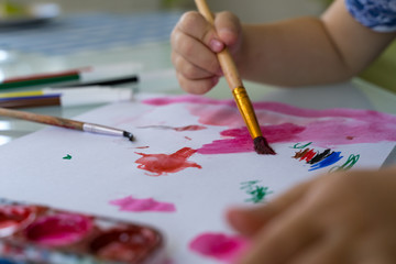 Naklejka premium child draws in watercolor on paper. brush in hand. preschool creativity