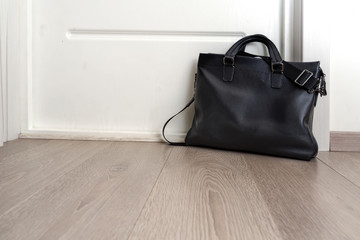 black leather briefcase stands near a white door