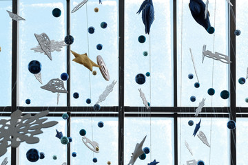 Christmas toys, balls and stars on the background of abstract glass windows. New Year decorations in a public place, supermarket, airport or shopping center. Winter holiday mood for design. Copyspace.