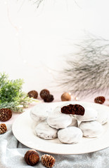 Chocolate cookies on a white plate on a background of fir cones and branches. Chocolate brownie cookies in white icing. Christmas gingerbread cookies. Holiday homemade baking.