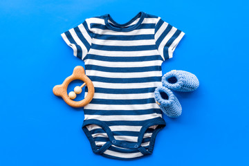 Blue bodysuit for baby boy near children's accessories on blue background top-down