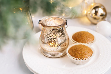 Delicious caramel muffins on a white plate with a golden candlestick lantern, on the background of Christmas decorations. New Year Christmas card.