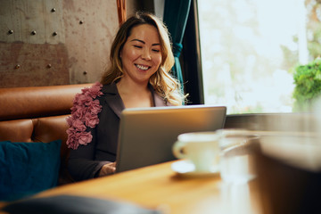 Beautiful Asian woman with laptop sitting in a cafe and smiling