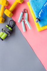 Gym equipment - dumbbells, jump rope - frame on grey and pink background top-down copy space