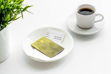 Paying in restaurant. Bank card near cup of coffee on white table