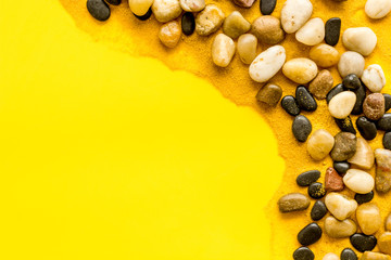 Sea rest, summer vacation concept. Stones and sand on yellow background top-down frame copy space