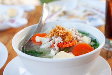 Clear Soup with Tofu and Minced Pork Thai people call Kang Jued Tao Hoo in a white bowl with spoon on dining table.