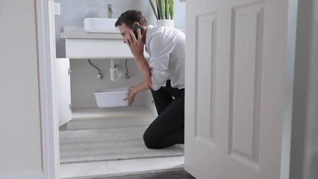 Man At Home Calling and Mopping Up Water From Leaking Pipe In Bathroom