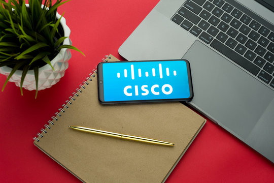 Tula, Russia, november 26, 2019: Cisco logo on the smartphone screen is placed on the Apple macbook keyboard on red desk background.